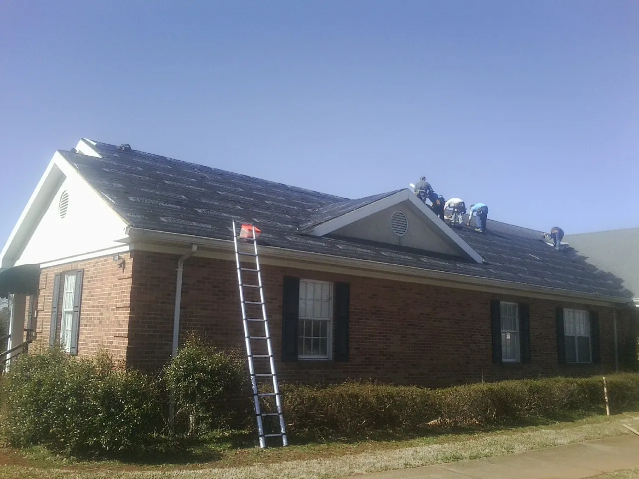 Crew tearing shingles off a brick ranch roof with a ladder set — Metal Roof Repair work by our crew in Westford