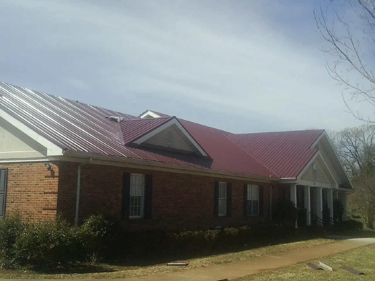 Red metal roof with gabled entries on a long brick building, from a Hail Damage Roof Repair job in Westford