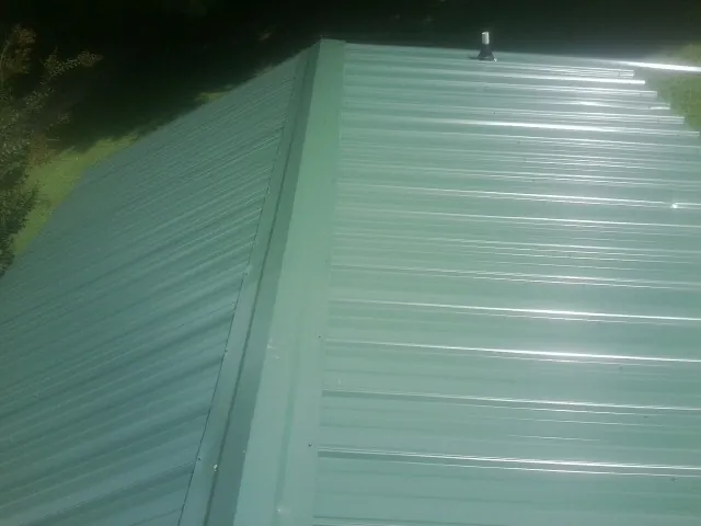 New green metal panels meeting at the ridge of a roof — Flat Roof Repair work by our crew in Westford