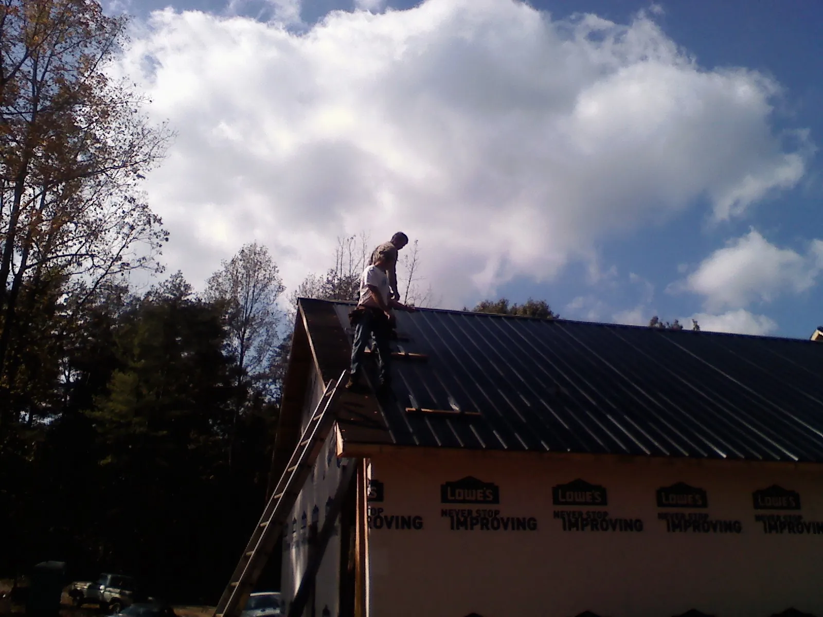 Roofer fastening dark metal panels high against a cloudy sky, from a Roof Inspection job in Westford