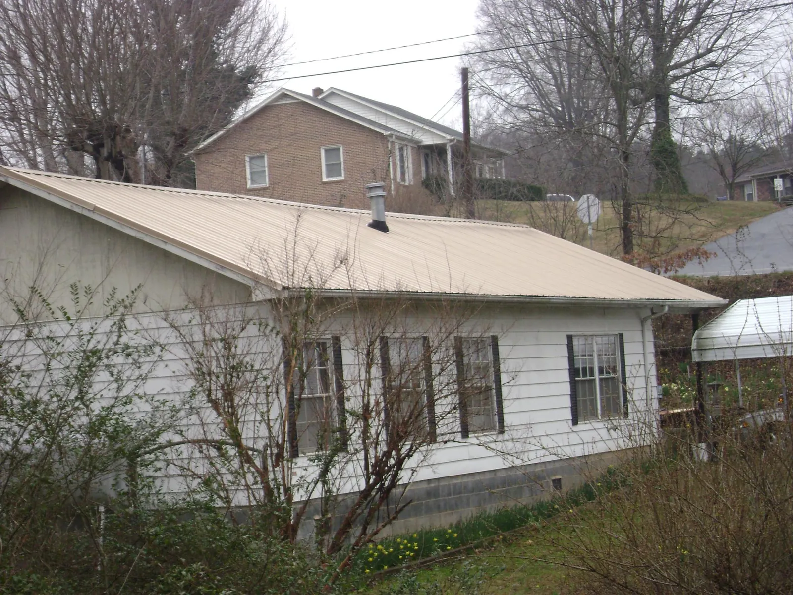 Tan metal roof on a white sided house set into a hillside — Commercial Roofing by Roofing Brothers in Westford