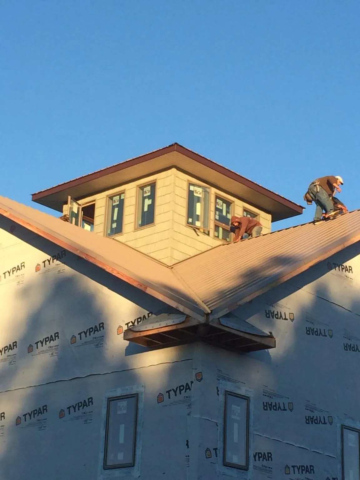 Roofers working around a rooftop cupola on a new metal roof at sunset — Roof Waterproofing in Westford by Roofing Brothers